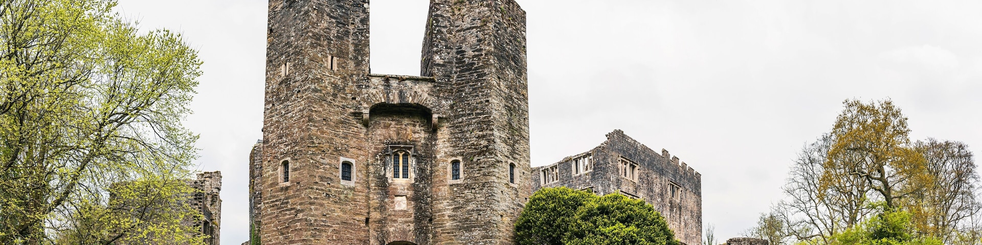 A historic stone castle with two prominent towers, surrounded by lush greenery and a well-maintained lawn.