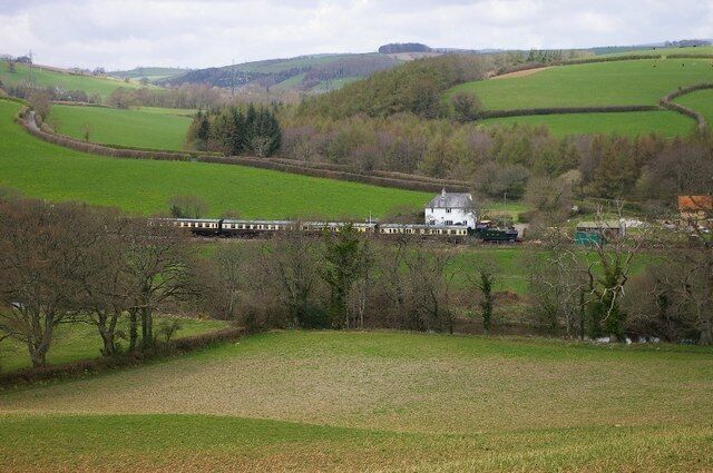 A white house on a hill, surrounded by green fields and trees.