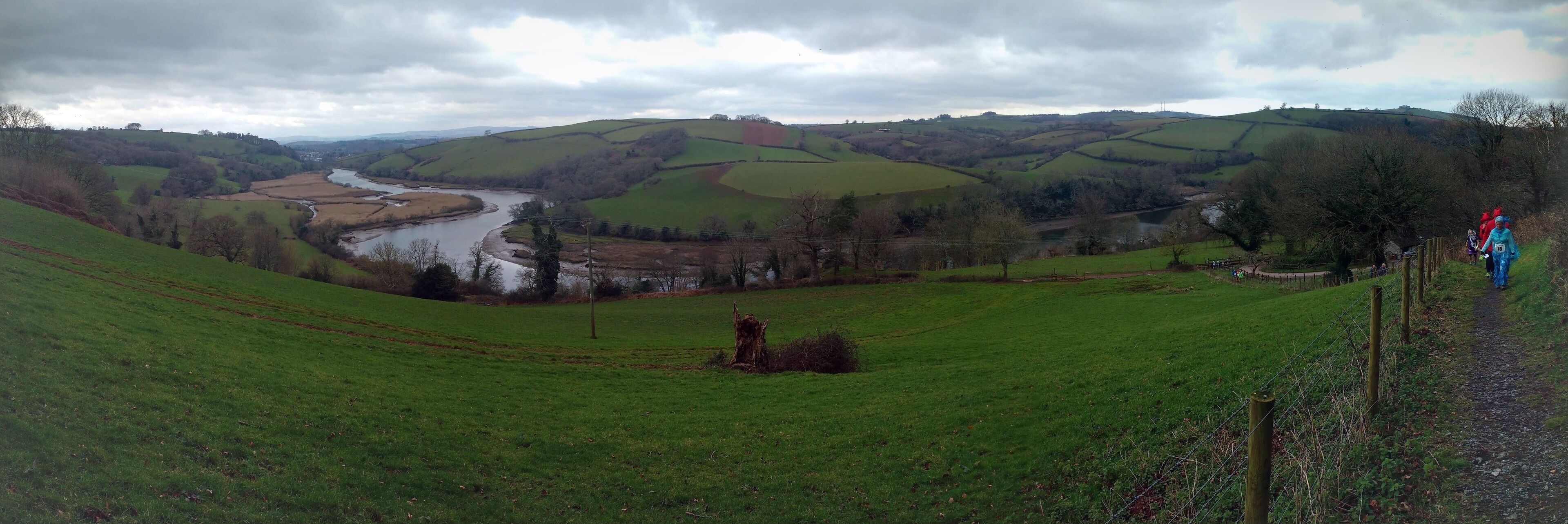 A green valley with a river, rolling hills, and a fence.