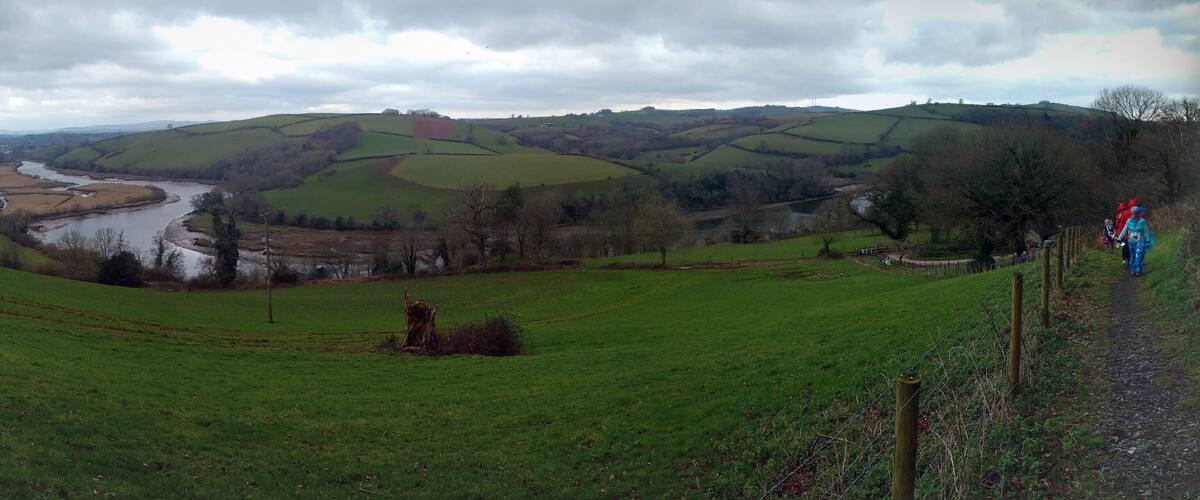A green valley with a river, rolling hills, and a fence.
