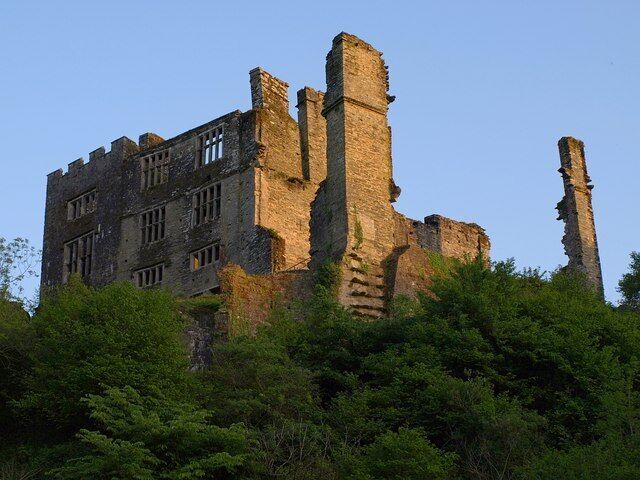 A large, historic stone castle with multiple towers and battlements, surrounded by dense green foliage.