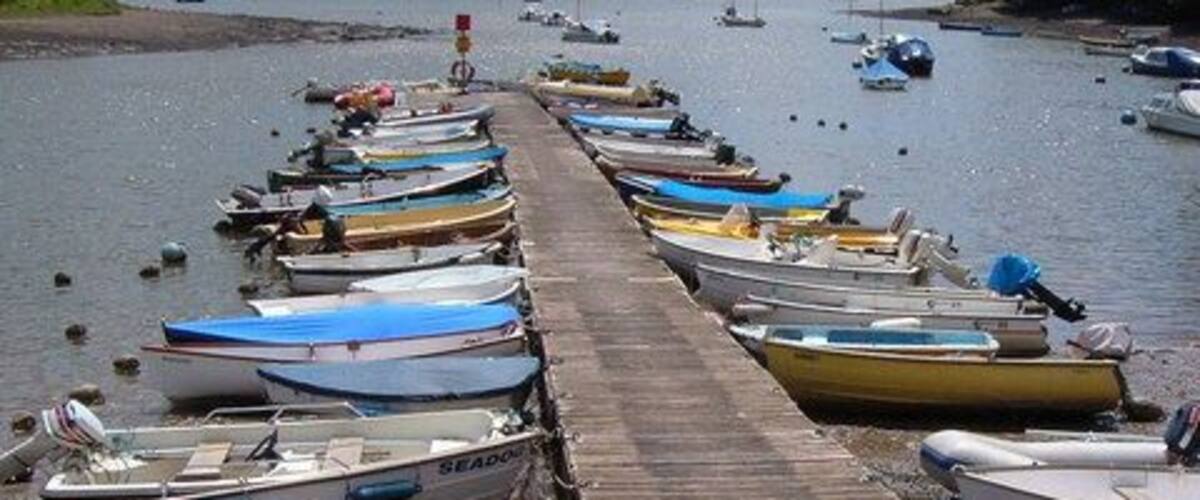 Pontoon, Stoke Gabriel. Looking down the pontoon with its moored boats from the edge of the dam that retains the mill pool. Beyond, the creek emerges into the main estuary of the River Dart, with fields below East Cornworthy on the far side.