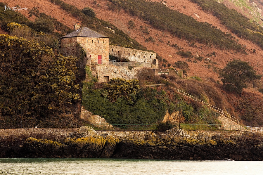 A stone castle on a hillside overlooking a body of water.