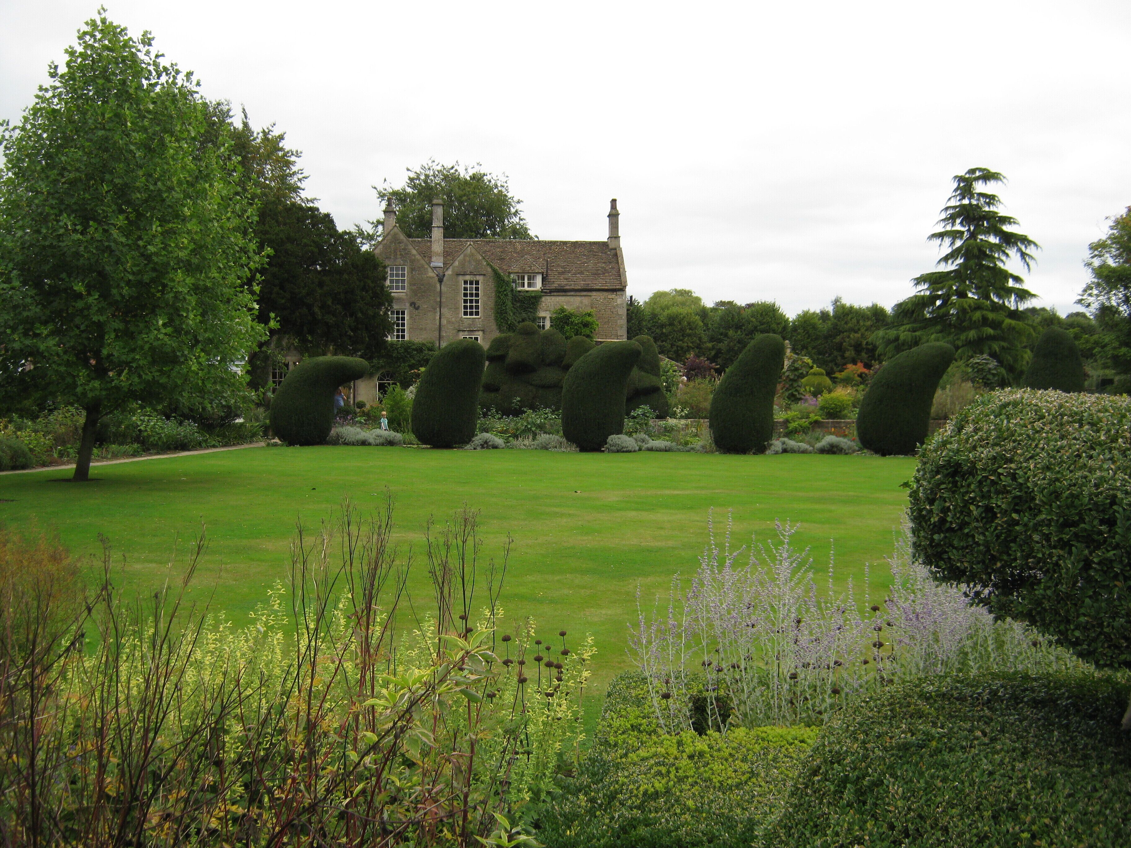 A well-manicured lawn, several topiary sculptures, and a large house in the background.