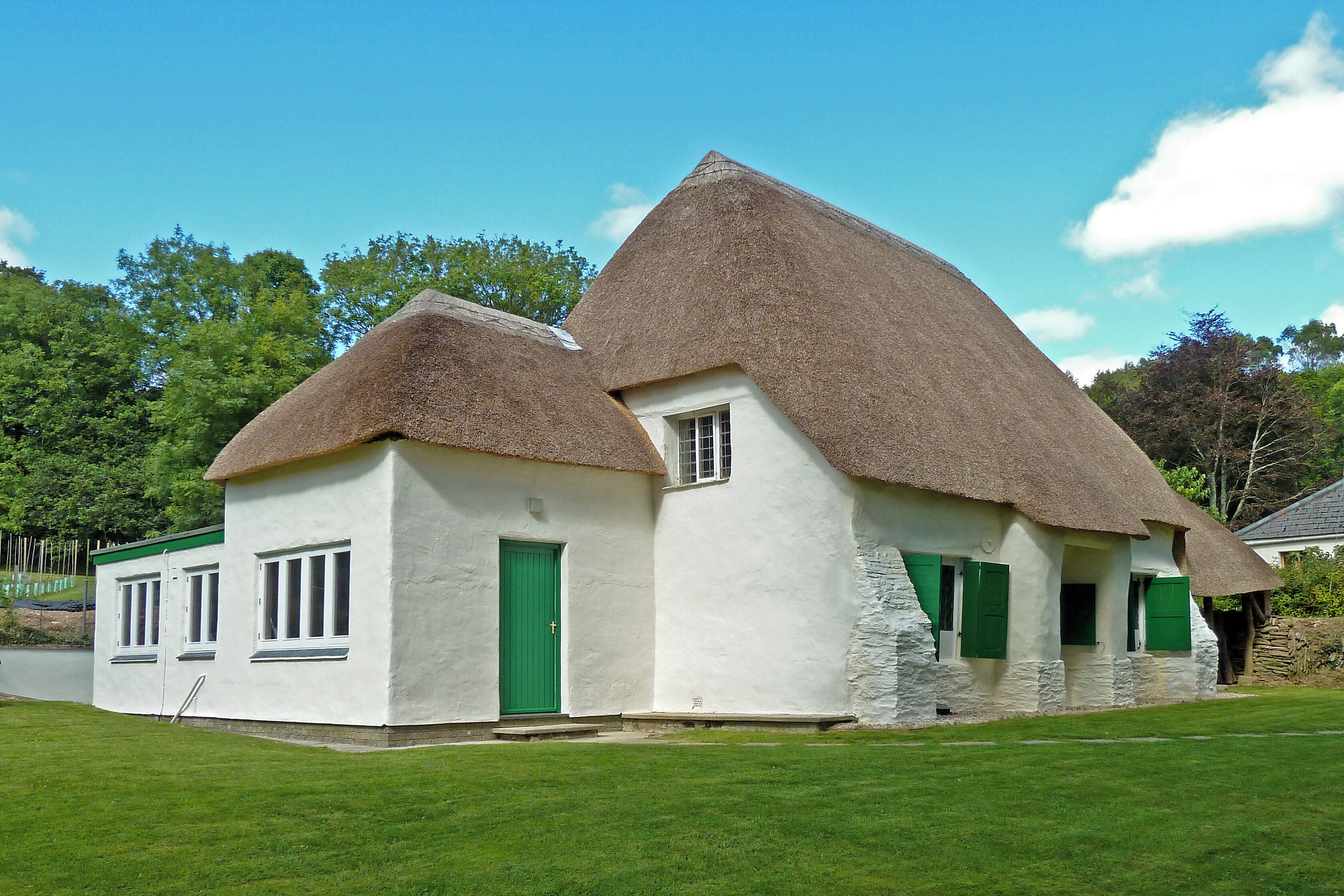 A white house with a thatched roof and green shutters.