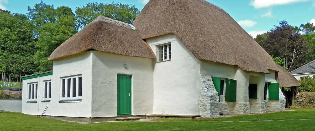 A white house with a thatched roof and green shutters.