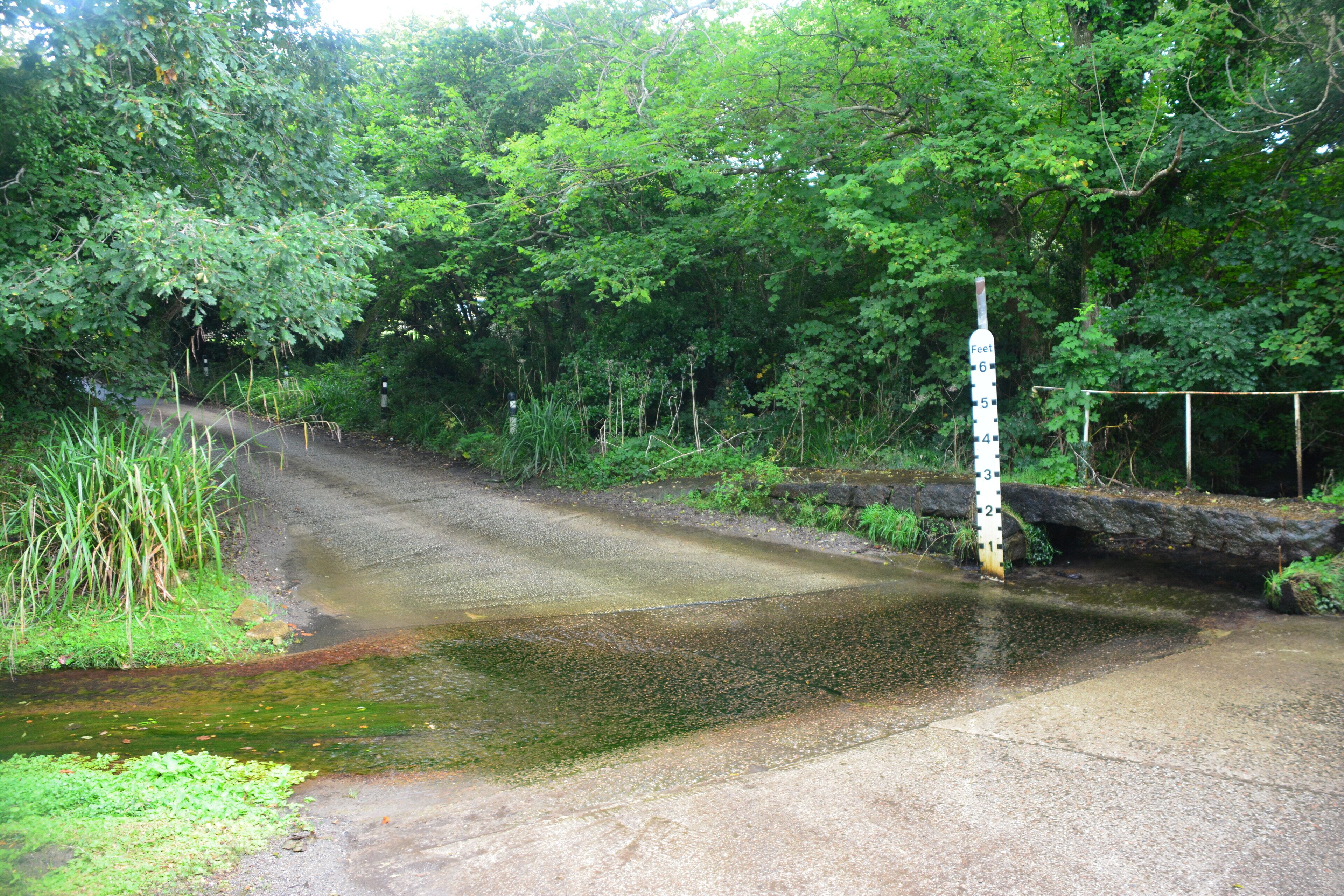 A narrow road crossing a shallow stream with a height marker.