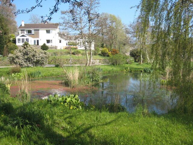A pond surrounded by lush greenery and a white house in the background.