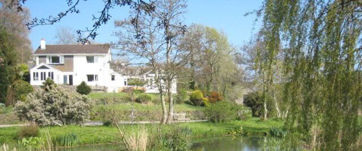 A pond surrounded by lush greenery and a white house in the background.