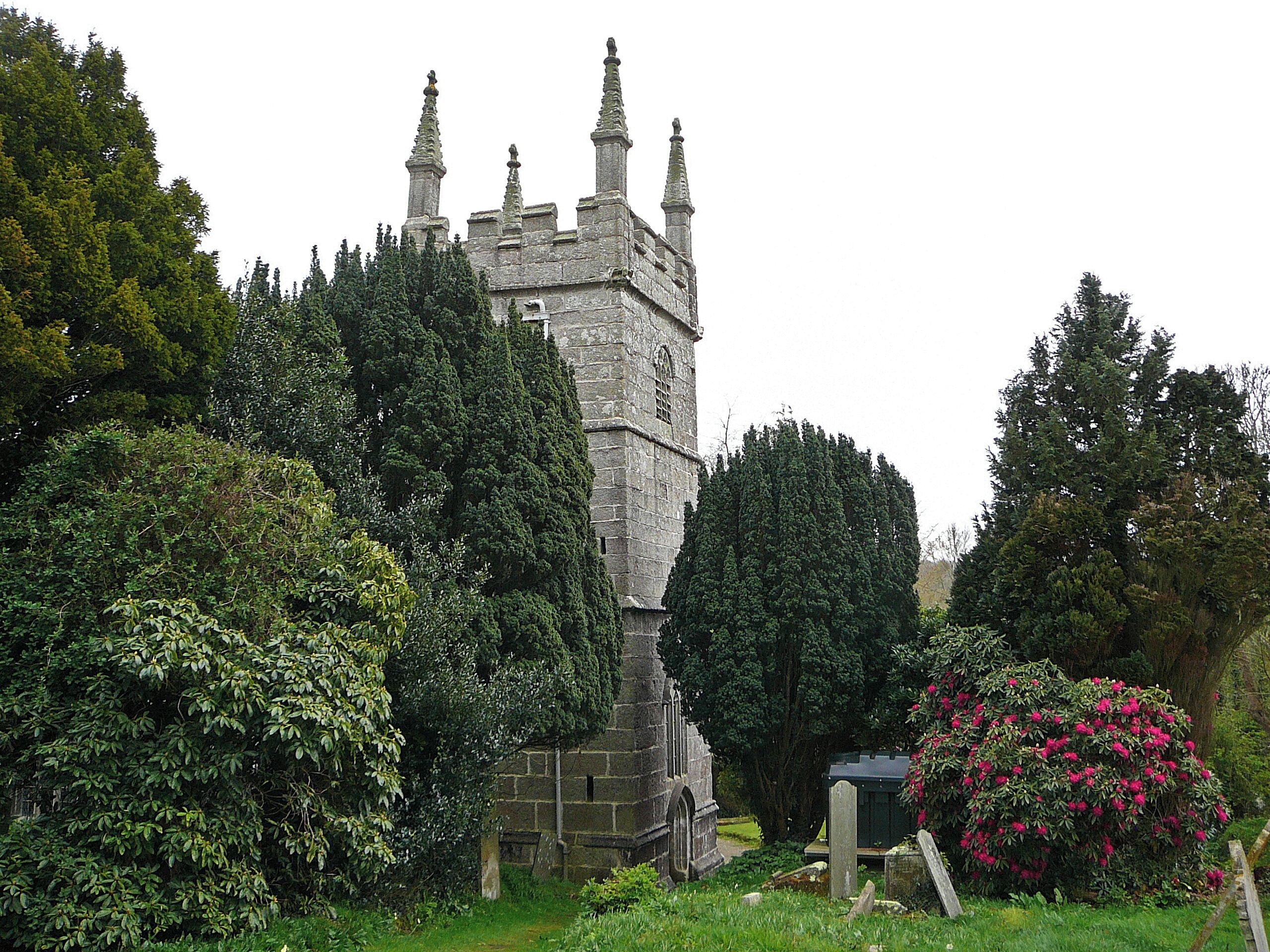A historic stone tower surrounded by lush greenery and a vibrant pink flowering bush.