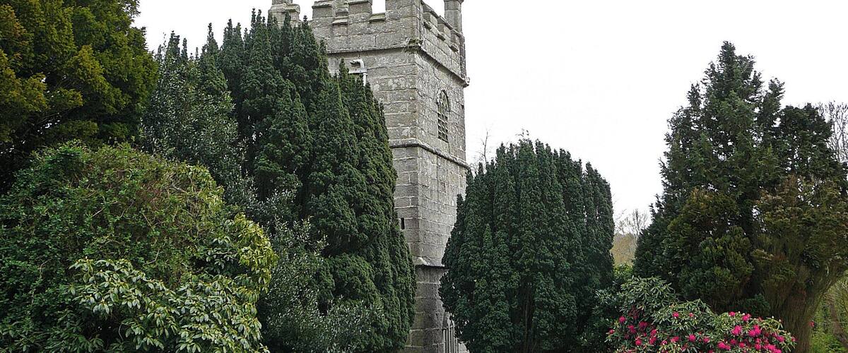 A historic stone tower surrounded by lush greenery and a vibrant pink flowering bush.