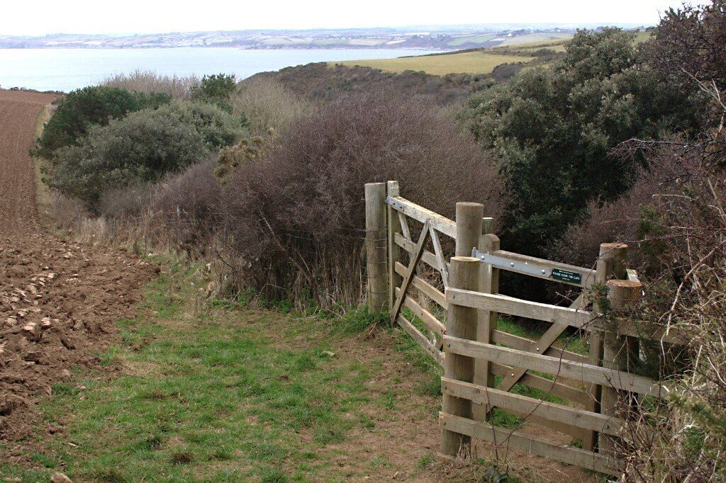 A wooden gate at the entrance of a rural path with a view of a lake and hills in the background.