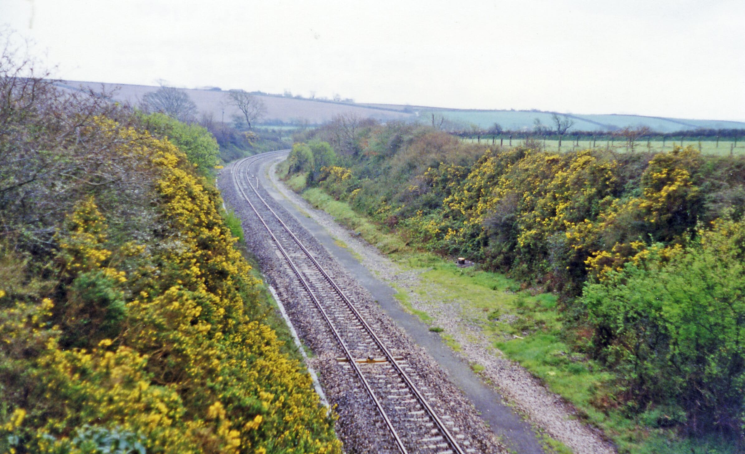 A railway track curving through a rural landscape with dense vegetation and fields.