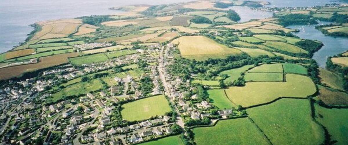 An aerial view of a coastal town with green fields, a river, and a sea in the background.