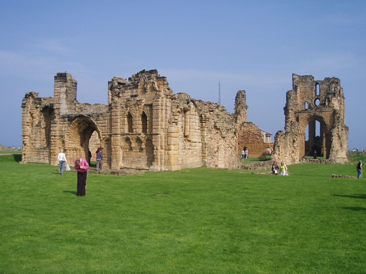An ancient stone structure with arches and ruins on a grassy field.