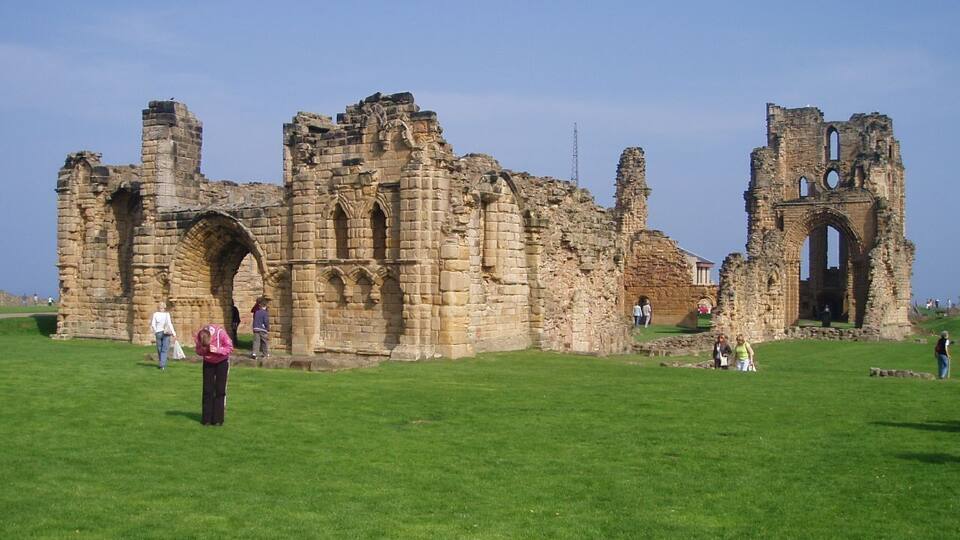 An ancient stone structure with arches and ruins on a grassy field.