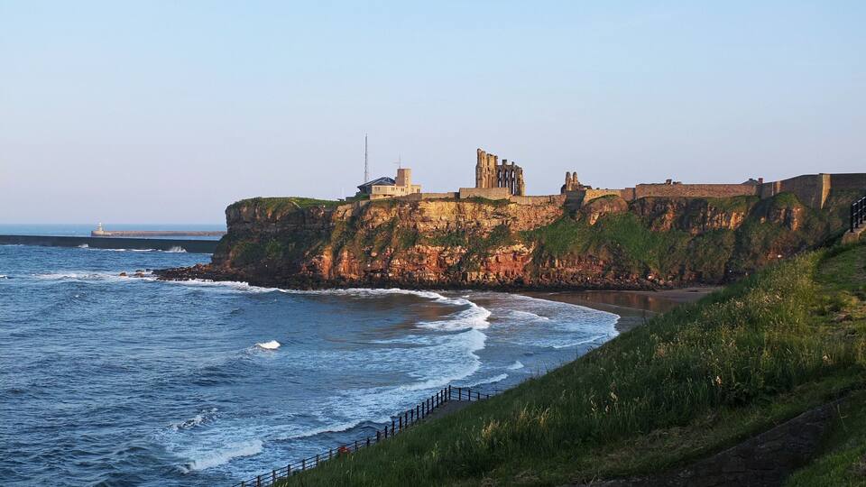 A coastal cliff with ruins and a lighthouse.