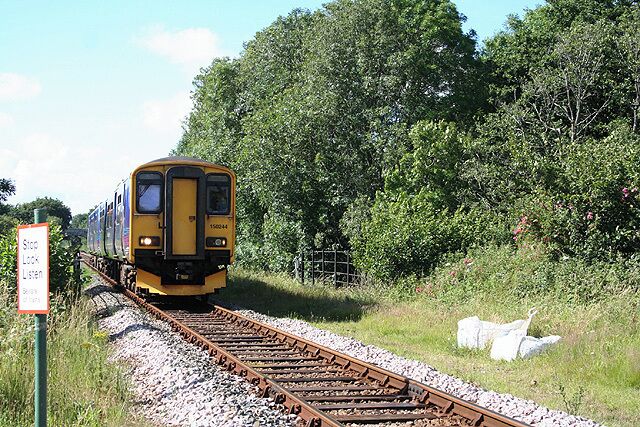 Tawstock: train on the Tarka Line Approaching, but not stopping, at Chapelton Station: a train from Barnstaple to Exeter crossing a bridge over the Langham Lake, a tributary of the river Taw.