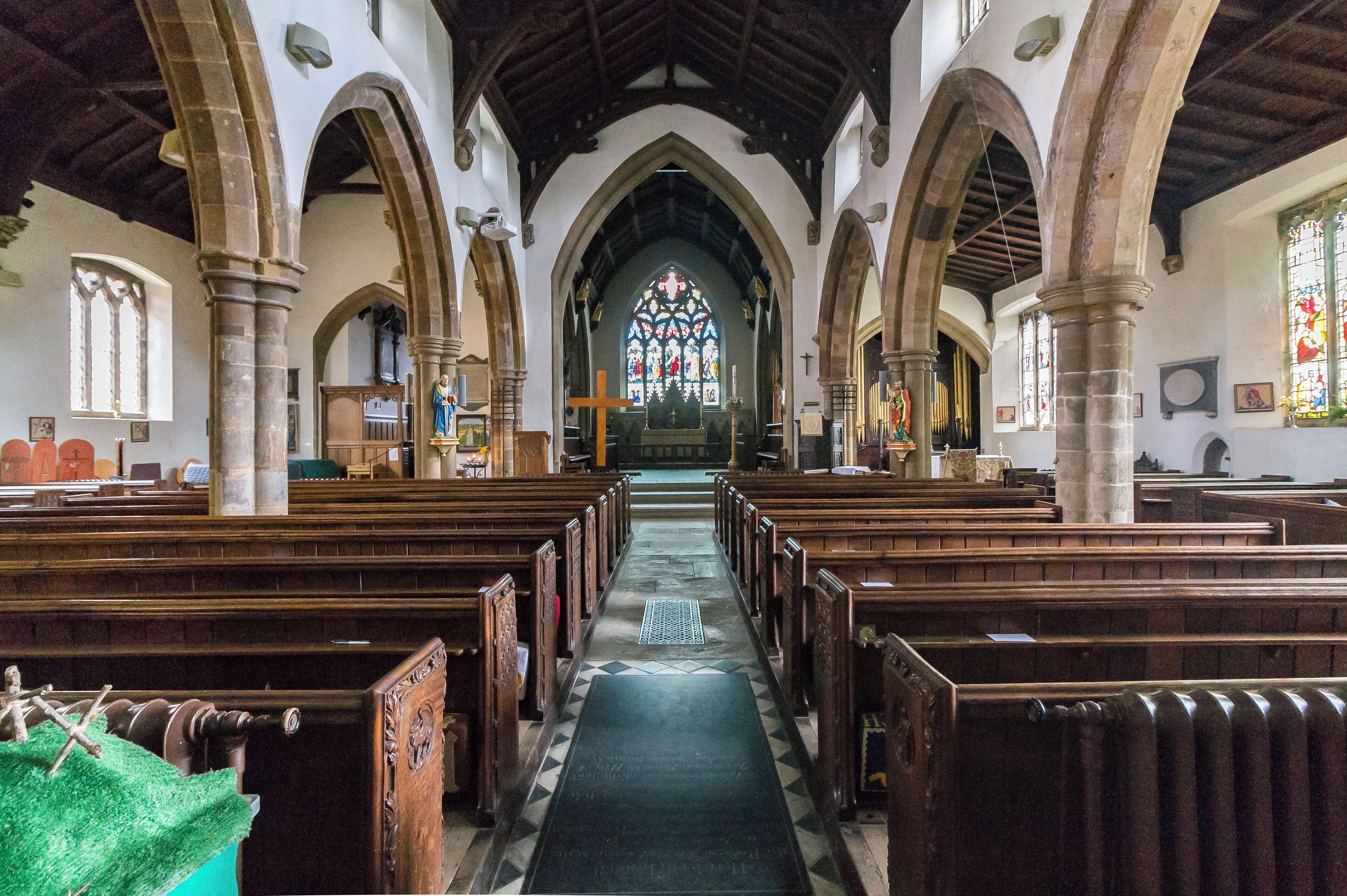 A church interior with wooden pews, a central aisle, and a stained glass window.