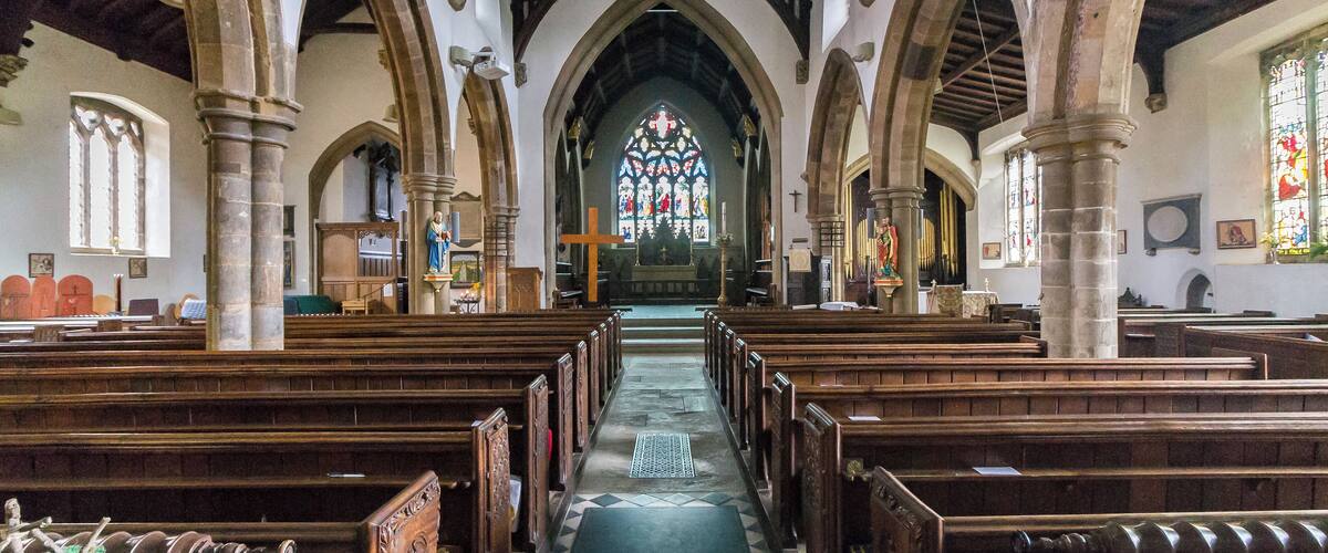A church interior with wooden pews, a central aisle, and a stained glass window.