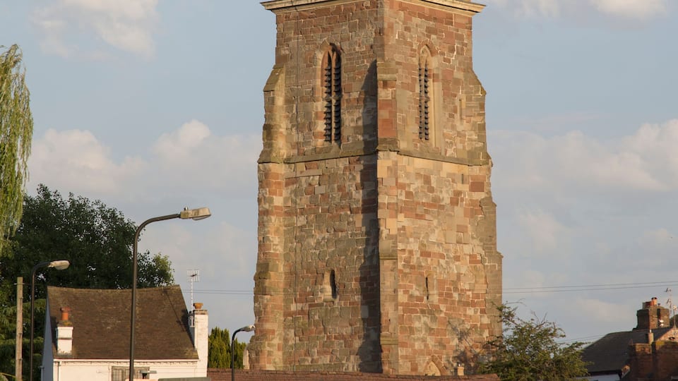 A historic stone tower with a green dome and a weather vane, surrounded by a small town with buildings and a street.
