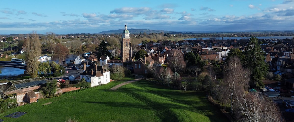 A town with a prominent clock tower, a river, and surrounding greenery.