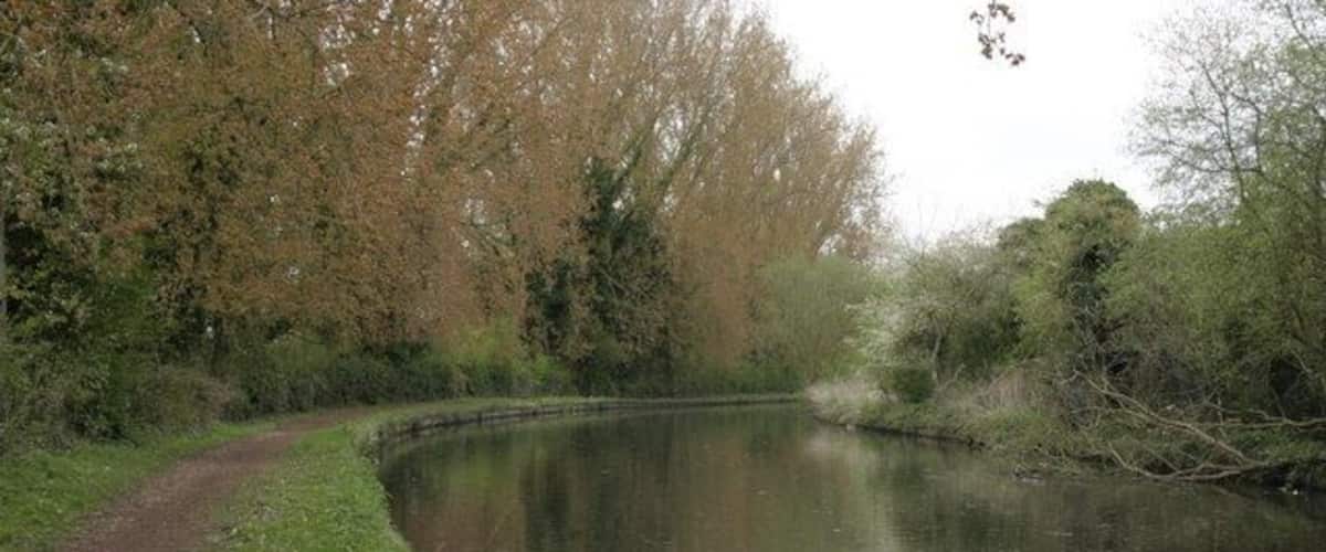 A curved canal with a dirt path on the left, surrounded by trees and greenery.