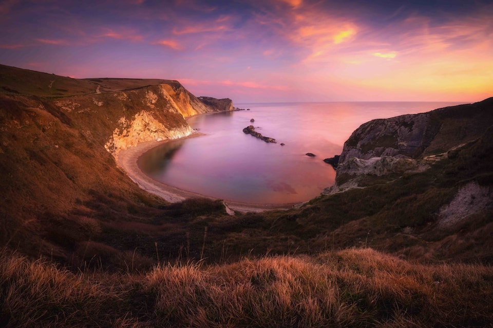 Un paysage côtier avec des falaises et une mer calme au coucher du soleil.