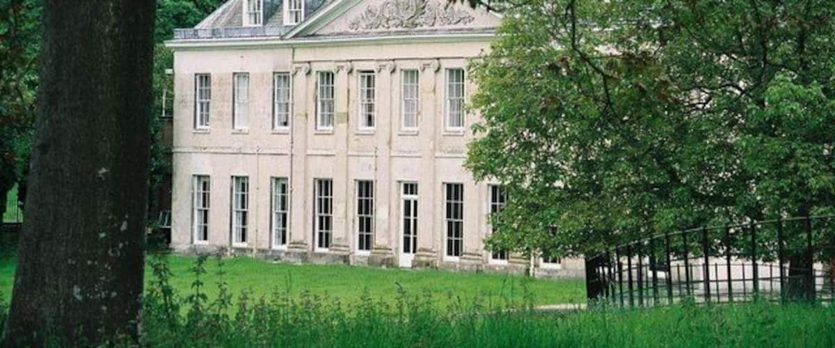 A large, classical building with symmetrical windows and a central entrance, surrounded by lush greenery.