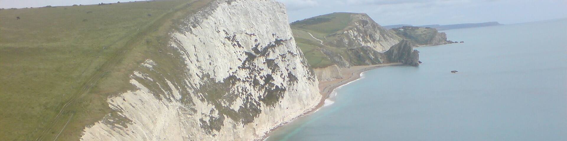 A coastal landscape with cliffs, a sandy beach, and a large rock formation in the water.