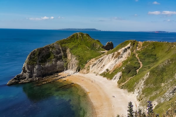 Eine Küstenlandschaft mit Sandstrand, felsigen Klippen und blauem Himmel.