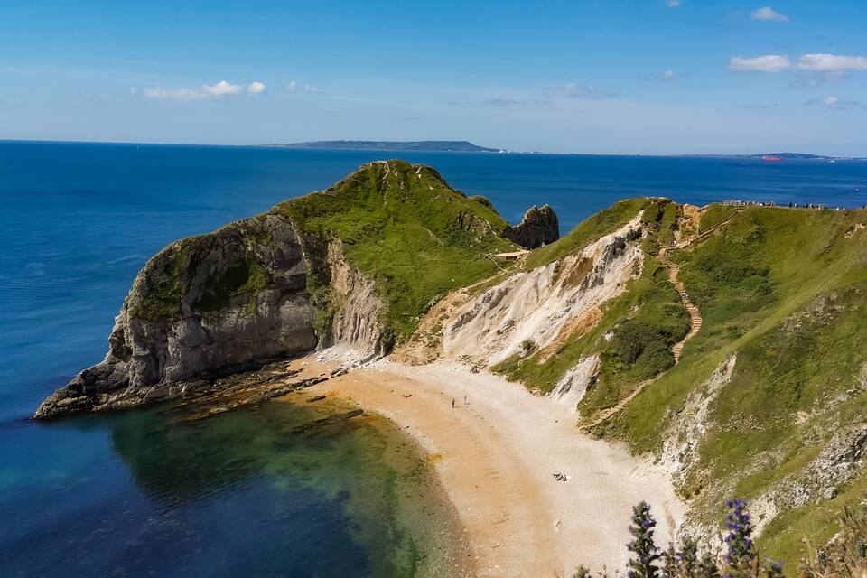 A coastal landscape with a sandy beach, rocky cliffs, and a clear blue sky.