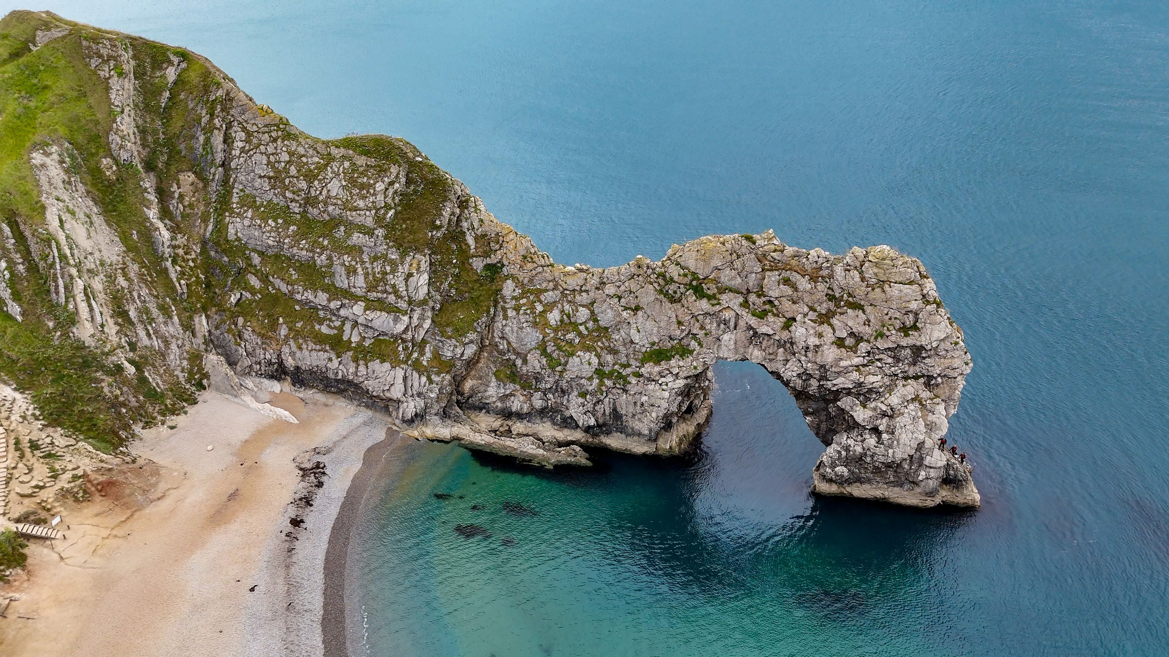Aerial view of Durdle Door, a natural limestone arch on the Jurassic Coast, with rugged cliffs, sandy beach, and deep blue sea in Wareham, England, United Kingdom.
