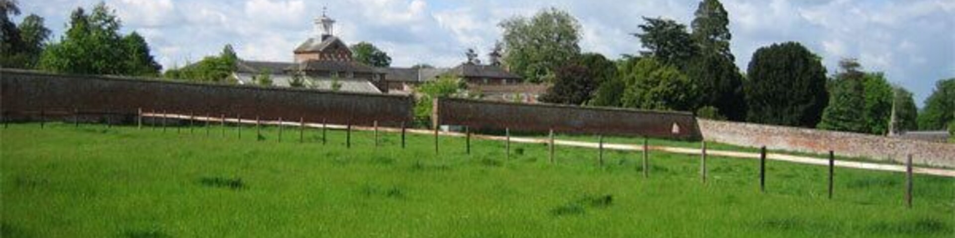 Un campo cubierto de césped con un muro de ladrillo y un edificio al fondo.