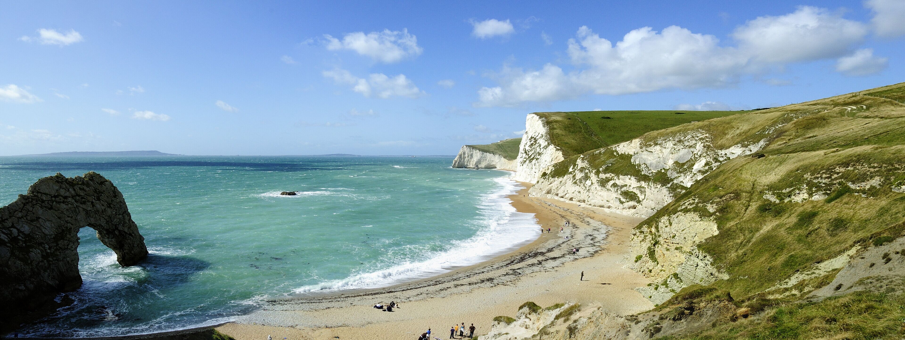 A coastal landscape with cliffs, a sandy beach, and a distinctive rock arch.