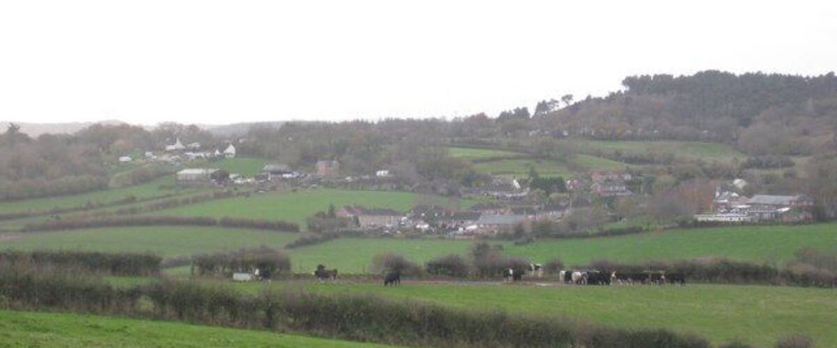 A rural landscape with rolling hills, fields, and scattered houses.