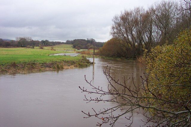 A flooded rural landscape with a river, trees, and open fields.