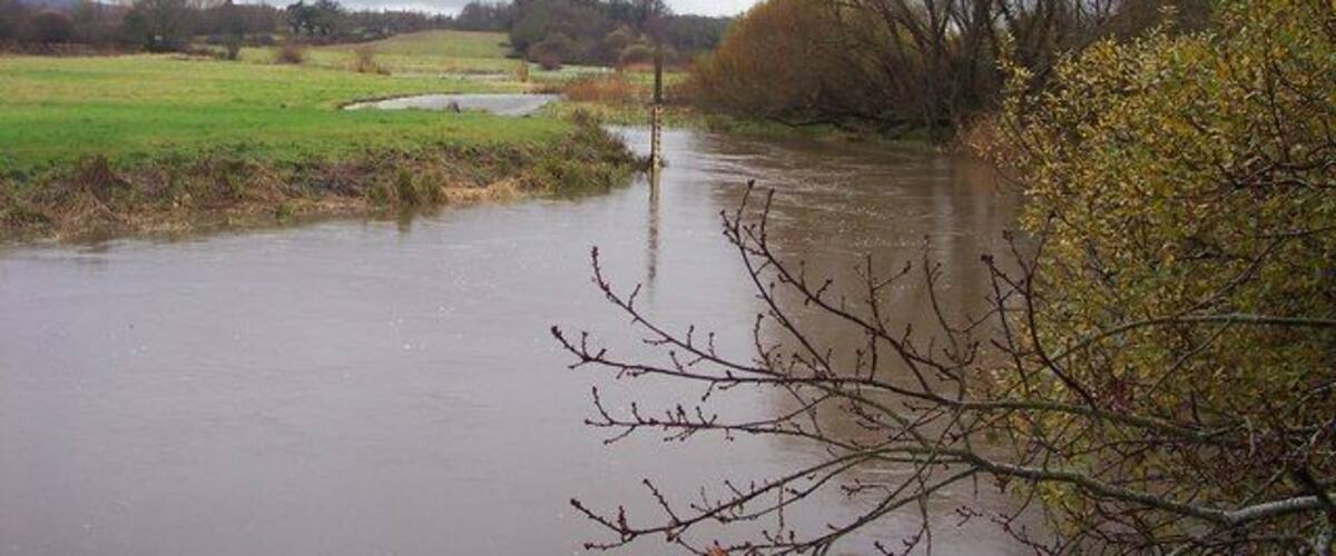 A flooded rural landscape with a river, trees, and open fields.