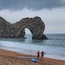 A rocky arch formation on a beach with two people standing nearby.
