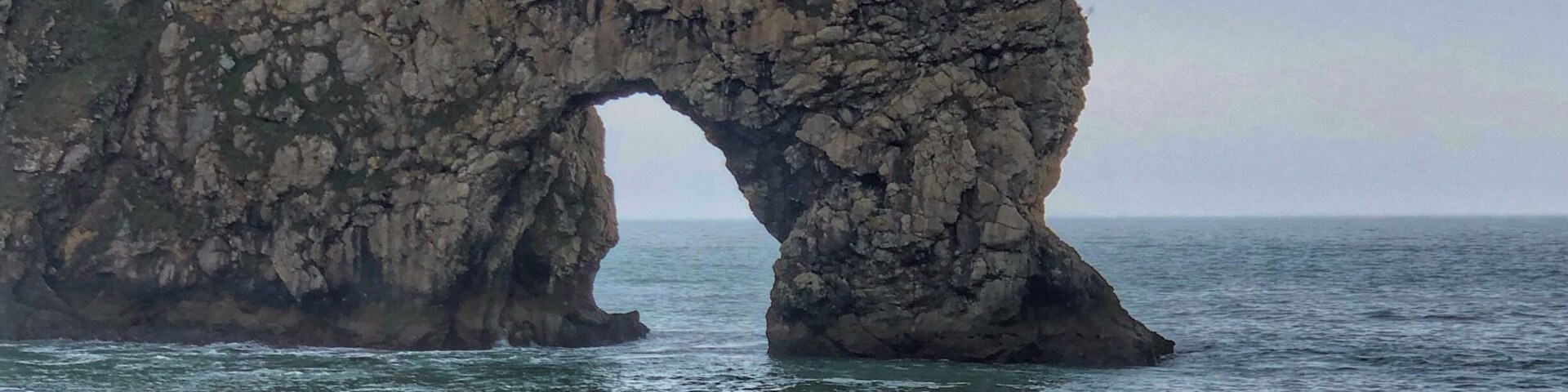 Une arche rocheuse naturelle se dresse sur une plage, et deux personnes se tiennent à proximité.