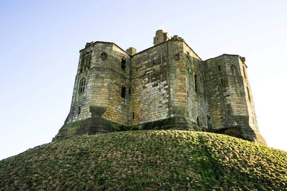 A historic stone castle with multiple towers, situated on a grassy hill.