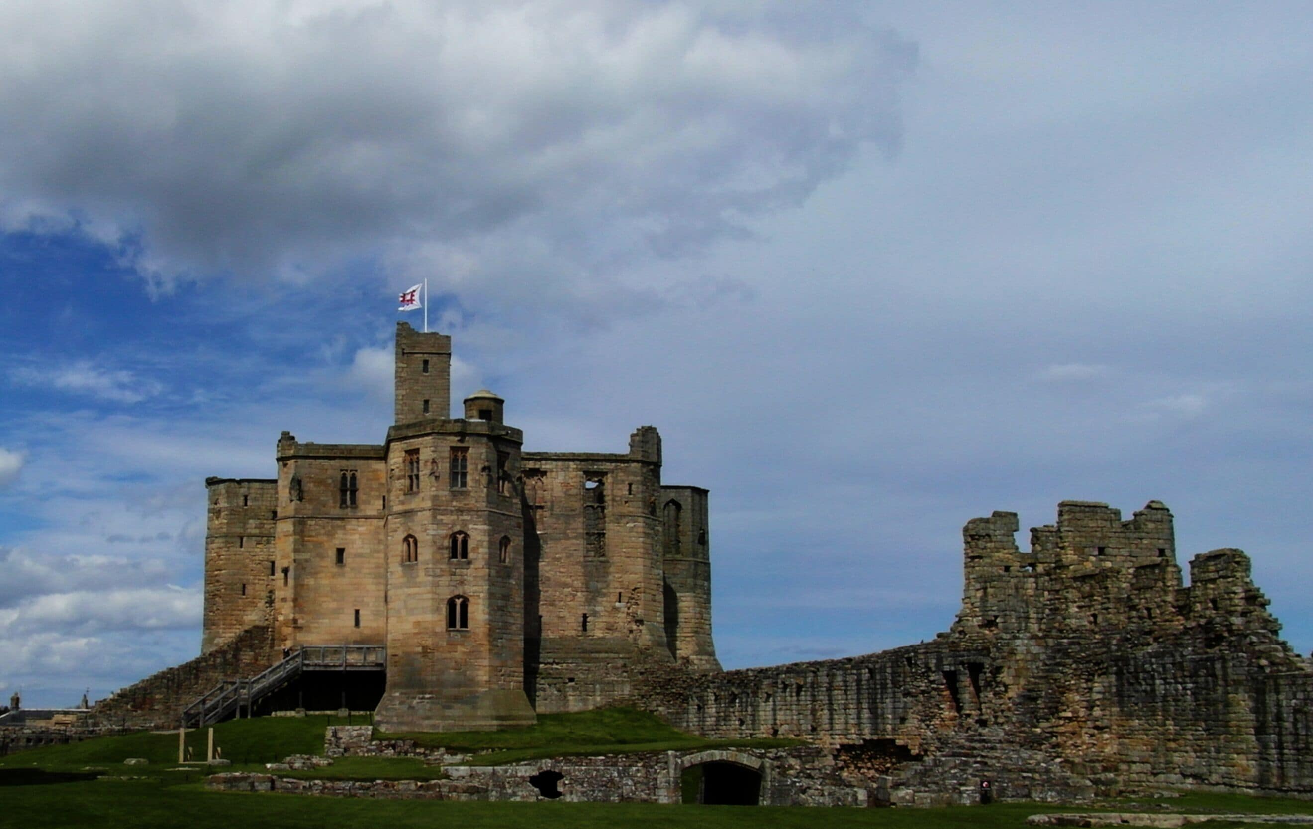 A historic castle with a flag, ruins, and a grassy foreground.