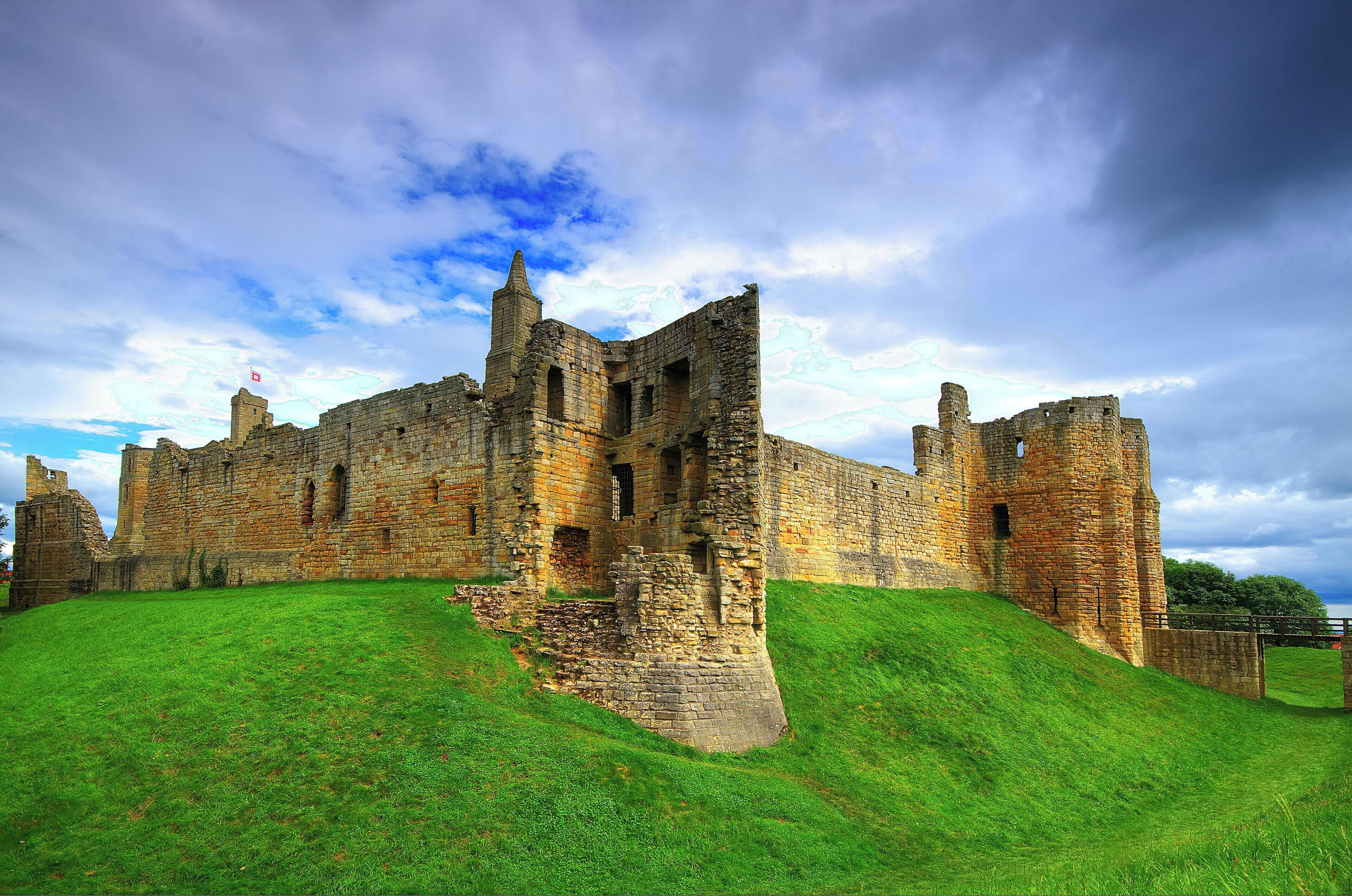 A historic castle with ruins on a grassy hill under a cloudy sky.