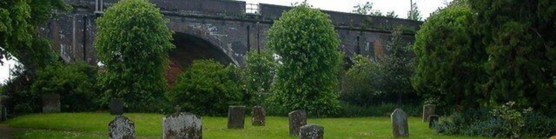 Un cementerio con lápidas, un puente y árboles al fondo.