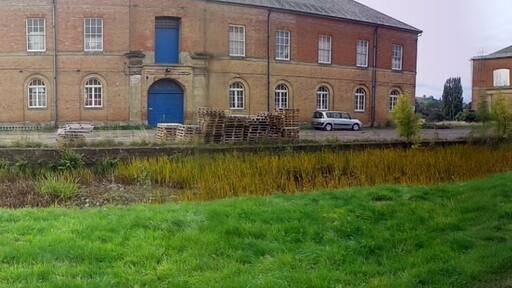 Former Ordnance Depot at Weedon Bec. The extensive barracks were begun in 1803 during the Napoleonic wars, but most of the buildings (including 12 powder magazines) have been demolished. This is a 180-degree panoramic shot and therefore the straight road appears as two roads. In fact it is parallel to the grass verge and canal in the foreground.