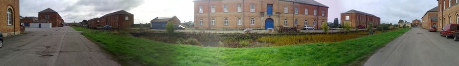 Former Ordnance Depot at Weedon Bec. The extensive barracks were begun in 1803 during the Napoleonic wars, but most of the buildings (including 12 powder magazines) have been demolished. This is a 180-degree panoramic shot and therefore the straight road appears as two roads. In fact it is parallel to the grass verge and canal in the foreground.