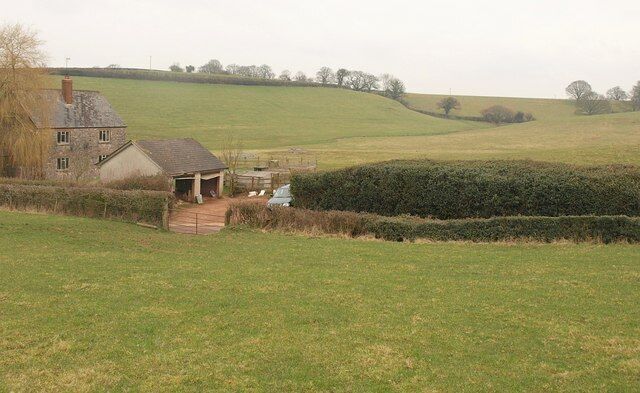 A rural landscape with a house, a small shed, and rolling green fields.