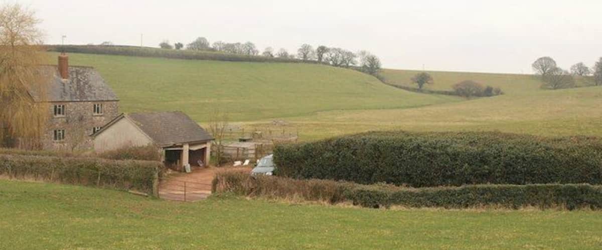 A rural landscape with a house, a small shed, and rolling green fields.
