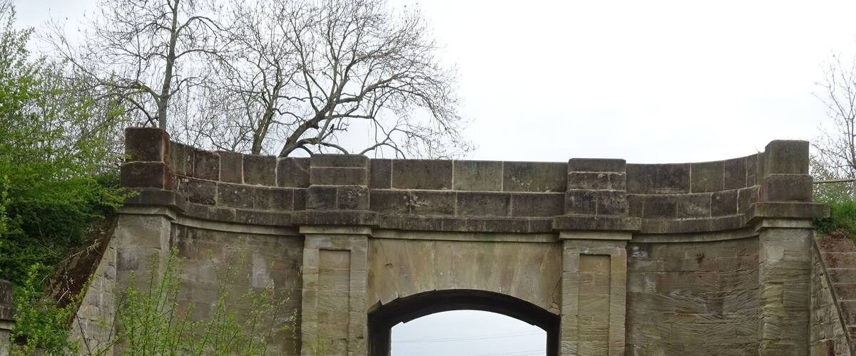 A stone arch bridge in a rural setting with a dirt path leading through it.