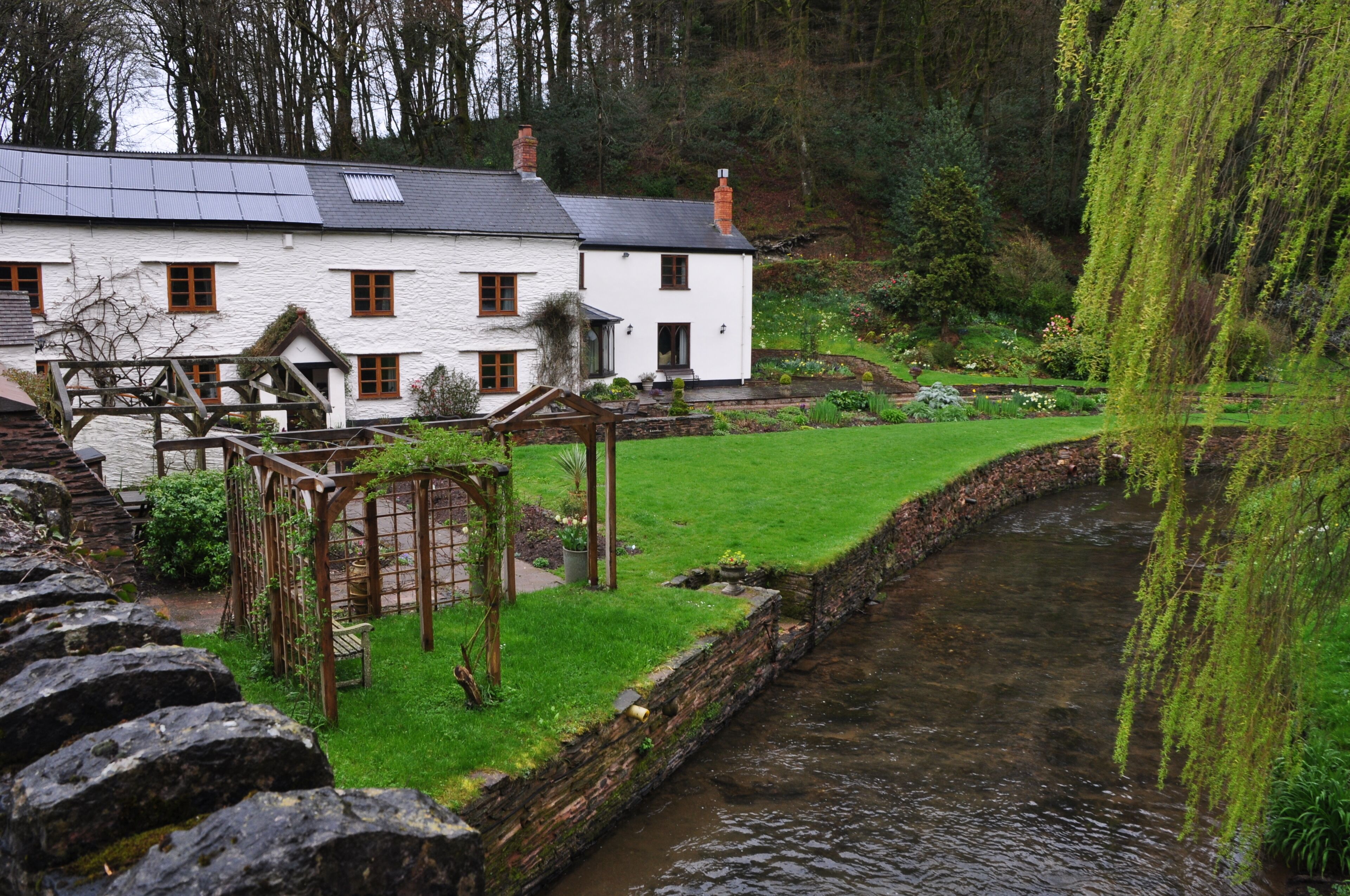 A white house with a garden and a stream.